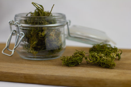 Dry medical marijuana lies in a glass jan with a lid on a wooden stand. Dried medical marijuana buds are stacked in a glass jar. Marijuana is used in medicine as a pain reliever for cancer.の写真素材