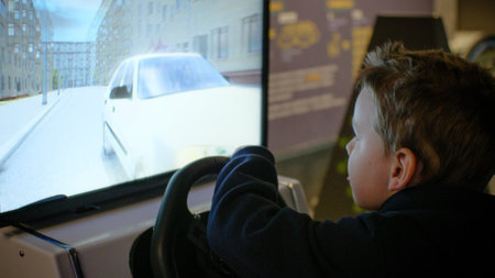 Child boy playing on a car simulator. Child driving a car simulator in front of a computer monitor. The boy drives a car in a computer game while driving. Child on the game machine.の写真素材