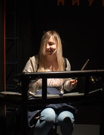 A lovely woman laughs merrily while sitting at a drum set with raised drumsticks in her hands The...