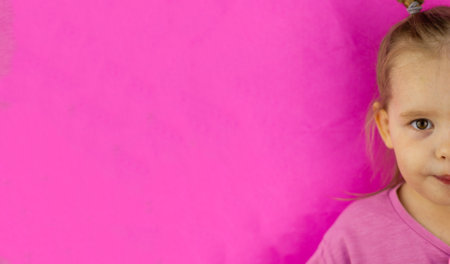 Half face of cute baby girl on pink background. Place to insert words or inscriptions. Beautiful caucasian baby girl on a pink background looks at the camera. Banner.の写真素材