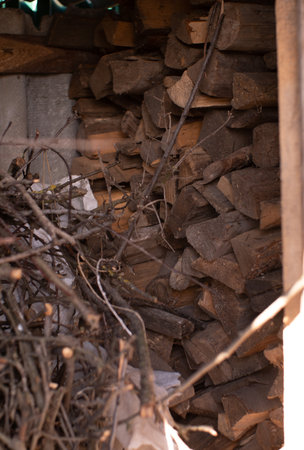 A pile of firewood stacked in neat rows near a brick wall. A stack of chopped firewood lies in a...