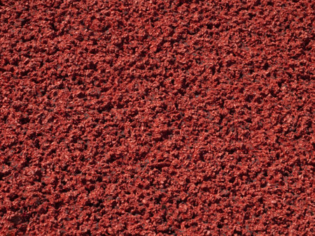 Textured background of a red sports surface on a running field. Rubber red granular coating on the sports field. Close-up background of a grainy rubber sports floor.の写真素材