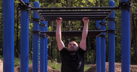 A handsome male athlete on a sports ground trains on the crossbars on a summer sunny day. A man...