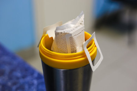 The filter bag with ground roasted coffee is installed on a thermo mug. Going on a trip, a person brews strong coffee from a filter bag. It is convenient to take coffee in filter bags with you.の写真素材
