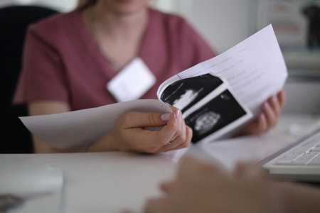 A woman doctor holds the results of an ultrasound examination in her hands and advises the patient. In the hospital, the doctor carefully examines the analysis of the ultrasound.の写真素材