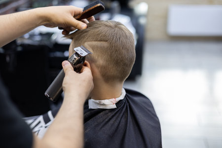 A professional hairdresser makes a drawing on the hair of a boys hair. The boy sits quietly in the chair of the barbershop and waits for the barber to finish the haircut with the pattern.の写真素材