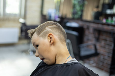 The child is trying to examine the hairstyle with a pattern in the hairdressers mirror. The child likes a beautiful hairstyle with a pattern. At the hairdressers, the child likes the new hairstyle.の写真素材