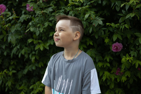 Portrait of a child standing against the background of green bushes with a pensive look A child in the summer stands against the backdrop of a hedge and looks to the side. Summer portrait of a child.の写真素材
