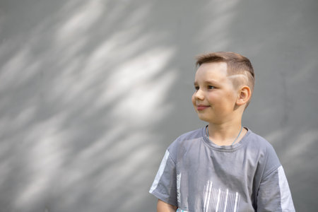 On a summer day, a child stands on the street against the background of a gray denmark wall....