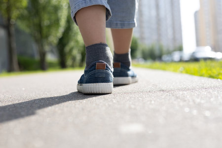 Childrens feet in boots are standing on the pavement in the sun. Close-up of childrens feet in boots in the summer on the sidewalk in the sun. The child is walking.の写真素材