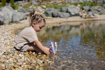 On a hot summer day a beautiful little girl sits at the waters edge on the shore Child on the beach on the shore of a beautiful lake with a beautiful view. Summer vacation with a child by the water.の写真素材