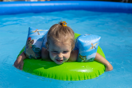 A cute little girl floats on an inflatable ring in the blue water of the pool. In summer, children enjoy swimming and playing in the water of the pool. The concept of children splashing in the water.の写真素材