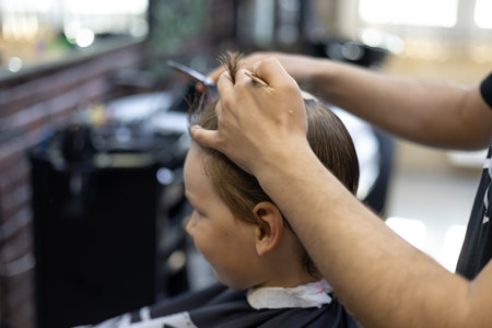 The hairdressers hands professionally trit the childs hair. The hairdresser combs the hair on the renkas head and cuts off the regrown ends. The concept of a child in a barbershop.の写真素材