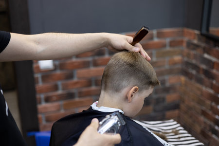 Tilting the boys head in front of the hairdresser straightens the edges of the hair. The hairdresser carefully treats the child while giving him a haircut. The concept of the work of a hairdresser.の写真素材