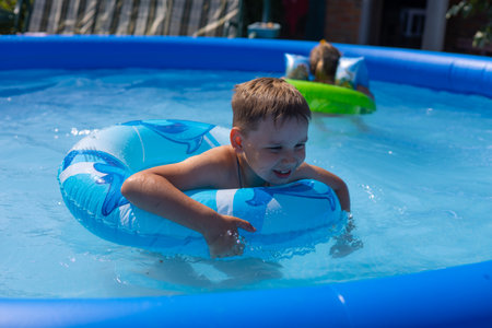 In summer, children swim in an inflatable pool with mugs and laugh. Children are enjoying the summer and splashing in the water of the pool in the backyard. The concept of children in the pool.の写真素材