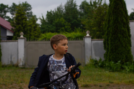 Child boy stands with a bicycle on a country road in summer in cloudy weather. The child after the rain decided to ride a bike through the puddles. The concept of a child with a bicycle.の写真素材