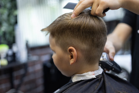 A child in a hairdresser does a hairstyle. The child sits quietly in the chair while the hairdresser works with scissors The hairdresser works in a hairdressing salon to make a hairstyle for a child.の写真素材