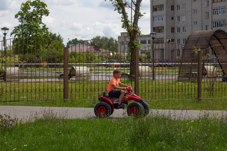 A child rides an electric quad bike in the summer in the park. During the holidays, the boy and his family rented an electric car for a ride. The concept of summer family vacation in the park.の写真素材