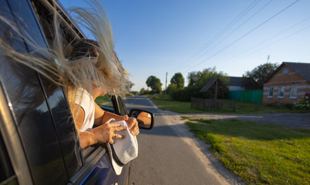 During a car ride, a beautiful woman leans out the window and enjoys freedom with flowing hair. On a clear summer day, a woman went on a trip by car. The concept of a sense of freedom.の写真素材