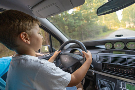 View from inside the car. The child sits on his fathers lap and learns to drive. The son is passionate about driving a car under the supervision of his father. Father and son concept.の写真素材