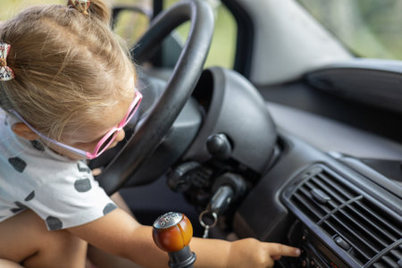 A small child plays with the buttons in the car while sitting behind the wheel on his fathers lap. Cute little girl playing with her father in the car. Father and daughter concept.の写真素材