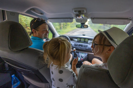 Happy family with a child in the car are discussing the upcoming trip. Parents happily look at their little child in the car. Family vacation concept.の写真素材