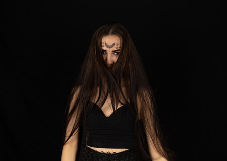 For halloween, a female witch stands in the dark with tousled hair falling over her face. Portrait...