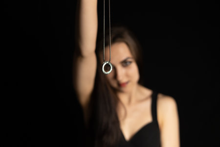 On Halloween in the dark, the witch hypnotizes the viewer with a talisman. A beautiful witch on a black background holds a magic talisman in her outstretched hand. Halloween concept.の写真素材