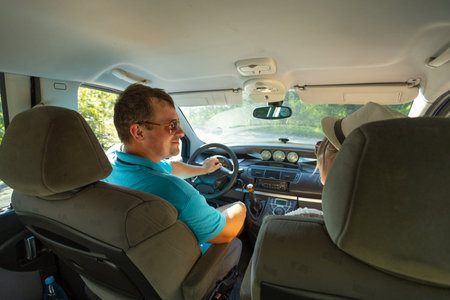 A beautiful couple of travelers sits in a car and joyfully looks at each other in anticipation of a long-awaited vacation. People travel by car. View from inside the car. Travel concept.の写真素材
