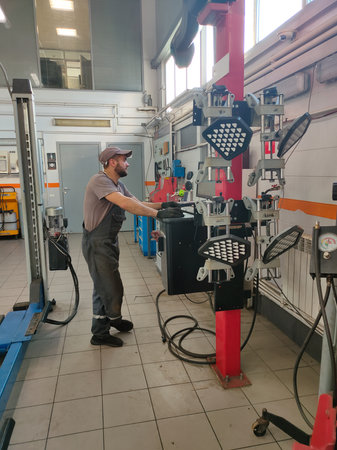 A male mechanic stands at a computer in a car service center and diagnoses a broken car that was brought in for repair. Computer diagnostics of a car in a workshop by a professional mechanic.の写真素材