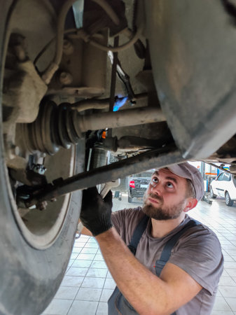 A mechanic in a car repair shop repairs the suspension of a car on a lift. A professional mechanic lifted the car onto a hydraulic lift to replace broken parts. Mechanic at work concept.の写真素材