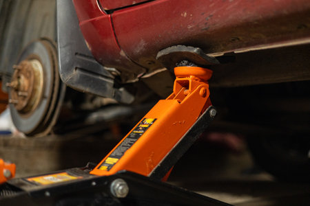 The car is standing in the garage, raised with a jack, while a man is repairing it Close-up of a jack under the bottom of a car in a garage. The jack holds the car while the person changes the wheel.の写真素材