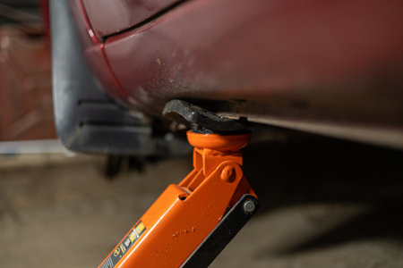 In the evening, in the garage, a man lifts the car with a jack to repair the brake disc. In the garage, a man is repairing his car himself. Concept of car repair in garage.の写真素材