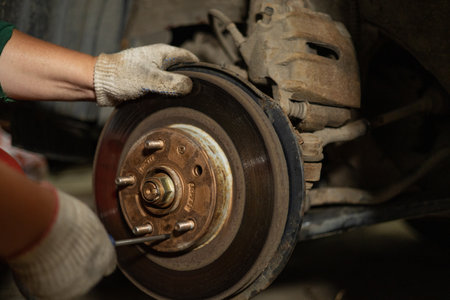 In the workshop, a male mechanic is changing the brake discs on a car. A man unscrews the bolts holding the brake disc with a screwdriver. concept of repairing a brake disc on a car.の写真素材