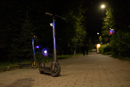An electric scooter stands on a city street at night. You can rent an electric scooter and quickly get to your desired location. Rent electric scooters in the evening in the city.の写真素材
