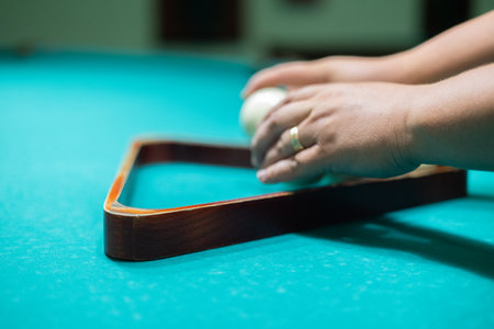 A mans hands stack billiard balls into a pyramid on a billiard table. A man collects balls into a...