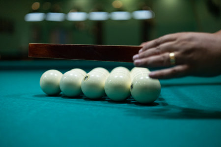 Having collected the billiard balls into a triangle, the man aligns them on the table and removes...