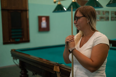 Copy space. A beautiful woman holding a billiard cue in her hands looks to the side, thinking about...