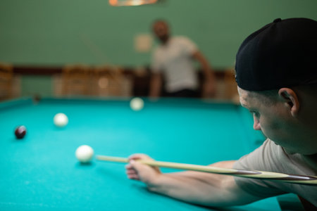 A group of friends plays billiards. The man hits the ball with a cue and hammers the meat into the...