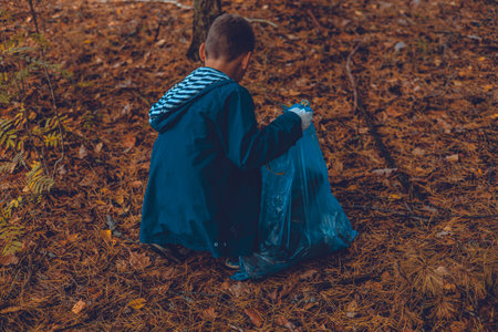 A child volunteer collects plastic waste in a garbage bag. A child eco activist saves the forest from plastic waste. Pollution of the planet with garbage, environmental problems.の写真素材