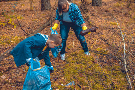 Eco activists mother and son walk through the forest with bags and collect garbage. Mom teaches her baby to take care of nature and save it from pollution by paste waste.の写真素材