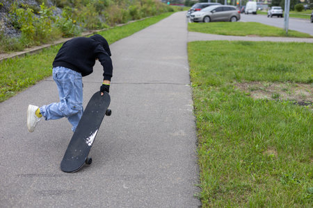 Copy space. On a city street, a stylish boy stands with a skateboard. A boy holds a skateboard with his hand during the day on the street among houses and cars. A child rides a skateboard.の写真素材