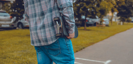 Close-up. Skateboard in a mans hand. A man carries a skateboard under his arm along a city street in...