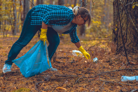 A female volunteer collects garbage in the forest. A woman is fighting to save a forest from being polluted by plastic waste. Eco activism. A woman walks through the forest and collects garbage.の写真素材