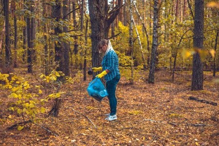 A woman volunteer collects plastic waste in the forest. A woman saves nature from being polluted by garbage. Environmental problems, plastic waste, environmental pollution.の写真素材
