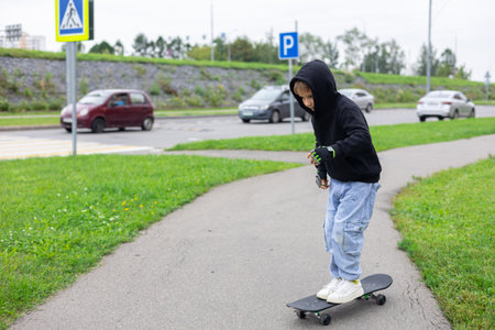 A boy learns to skateboard on a city sidewalk. A hipster boy kicks off and rushes along a city street on a skateboard. Lifestyle. The childs hobby is extreme sport, skateboarding.の写真素材