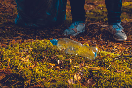 A plastic bottle lies on the moss in the sun. In the forest, a woman volunteer came up with a...