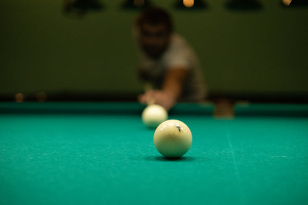 A man plays billiards and prepares to hit. A man aims his cue at a billiard ball while leaning towards the table. In the evening, a man relaxes after work by playing billiards.の写真素材