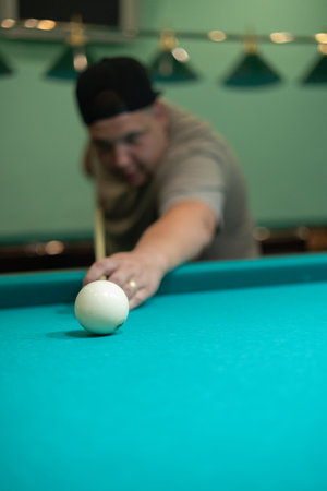 A man aims a cue at a billiard ball on a green table. A man hits a billiard ball and tries to pocket it. A man plays Russian billiards with his friends. Concept of a man playing billiards.の写真素材