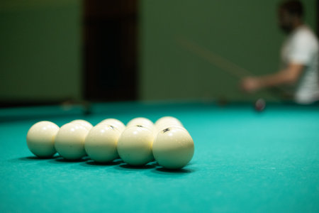 A group of friends plays billiards. The man hits the ball with a cue and hammers the meat into the pocket. People have fun playing billiards in the evening. Concept of a company playing billiards.の写真素材